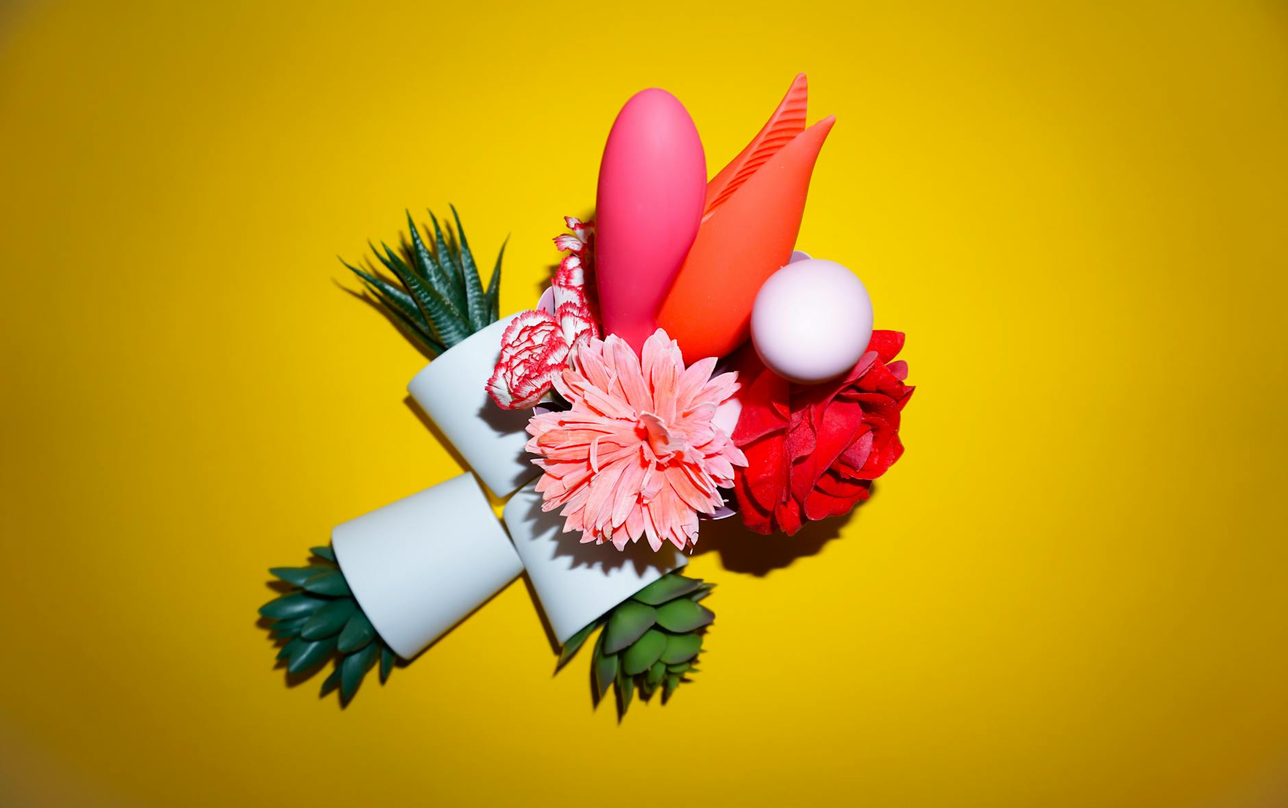 Vibradores coloridos com flores em uma bolsa de presente holográfica contra fundo amarelo vibrante